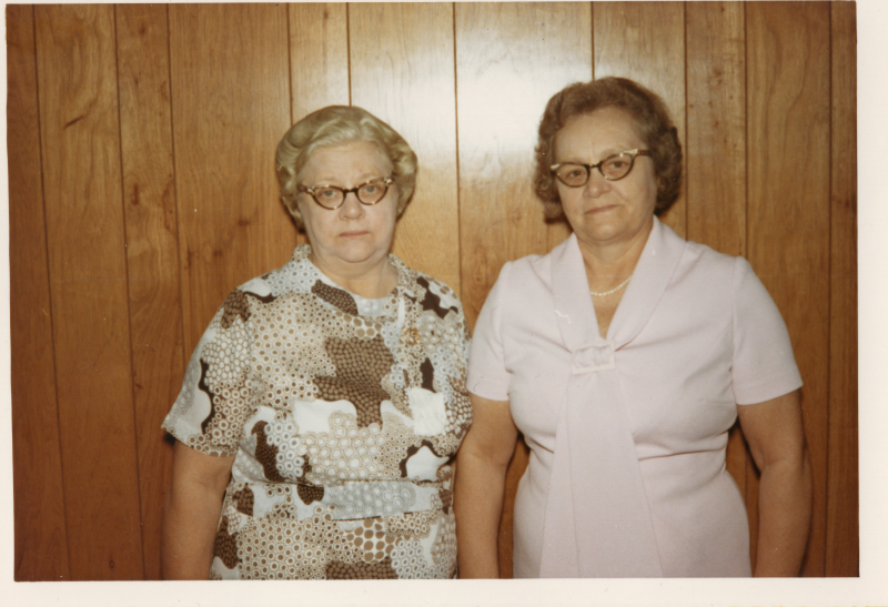 Two women pose in front of a wood panel wall