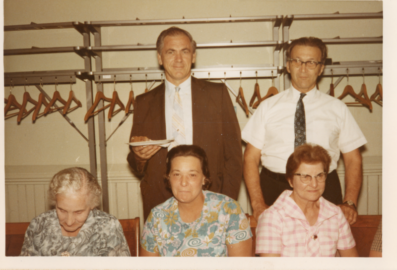 Two standing men smile behind three seated women