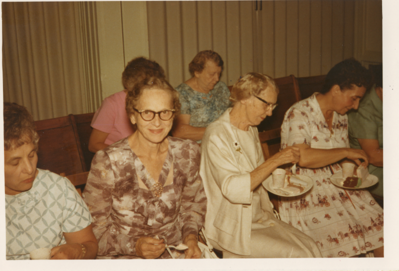 A woman smiles at the camera as other women enjoy refreshments