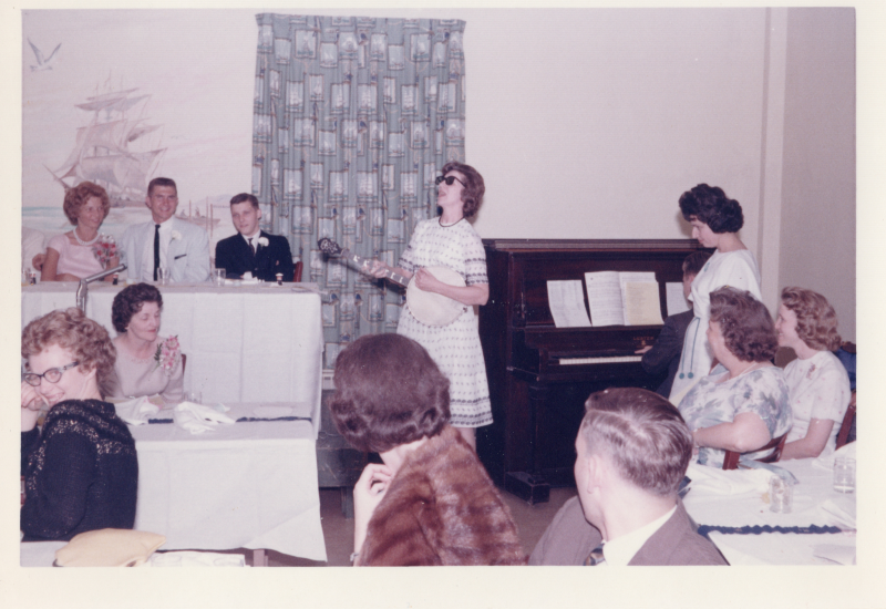 A woman in sunglasses plays a banjo while a crowd watches
