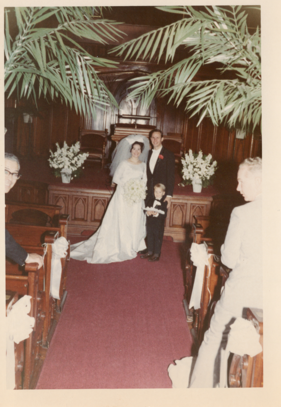 Bride and groom are surrounded with foliage in the sanctuary, and pose for a photograph with a young ringbearer