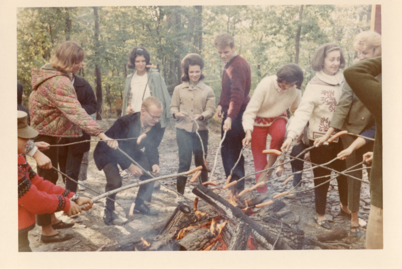 A group roasts hotdogs around a campfire
