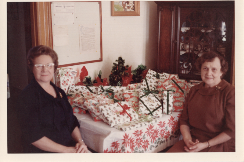 Two women seated with a table of wrapped Christmas presents