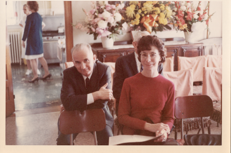 A seated man and woman smile for a photograph with flowers in the background
