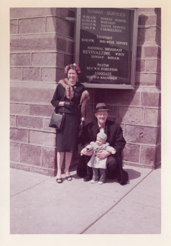 A man, woman, and baby smile in front of a sign that lists Highway's upcoming services