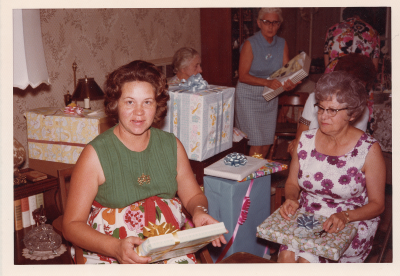 Two women are seated with several wrapped presents