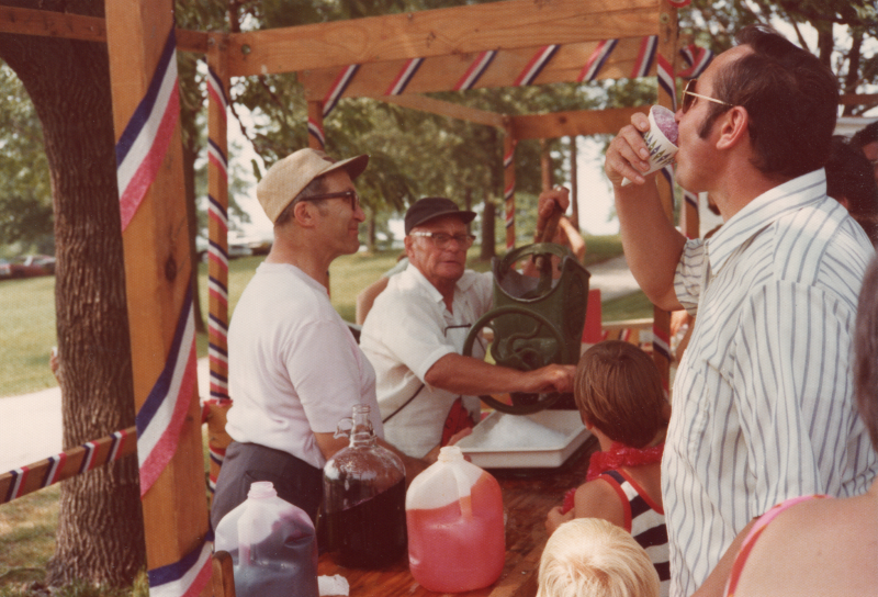 A group congregates at an outdoor refreshments table with streamers