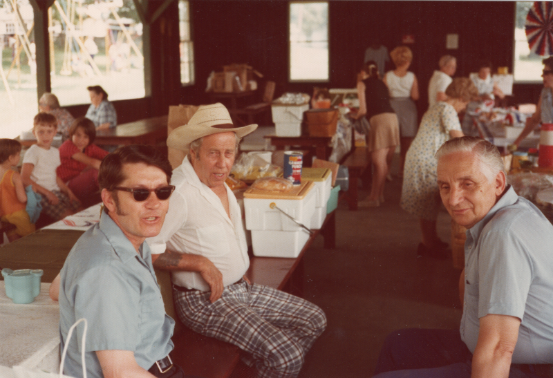 A group of men sit at picnic tables talking