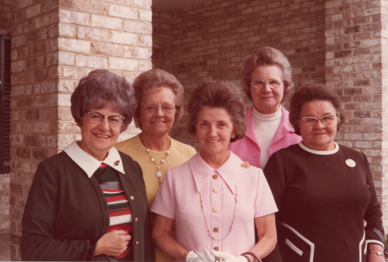 Five older women pose for a photograph outside