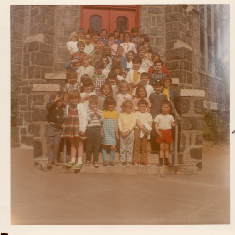 A group of children stand for a photograph on steps in front of a red door