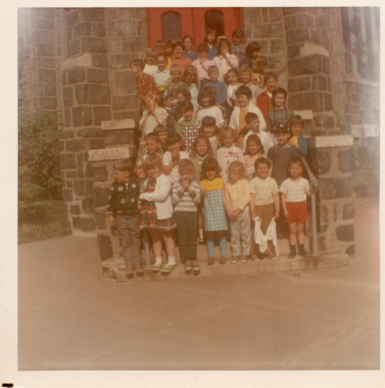 A group of children stand for a photograph on steps in front of a red door