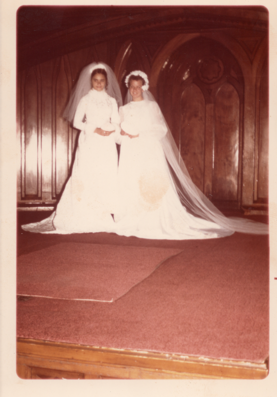 Two young women wearing wedding gowns and veils pose for a photograph on stage in sanctuary
