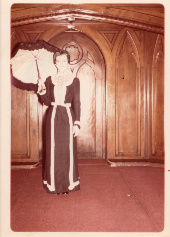 A young woman wearing a black gown and carrying a black parasol poses for a photo on the sanctuary stage