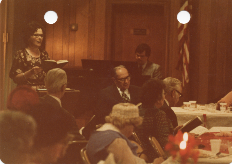 Mrs. Stone leads a hymn while a man plays a piano