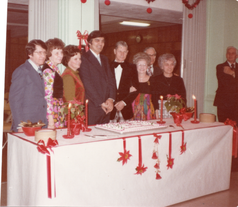 A group of people stand in front of a cake with Christmas decorations