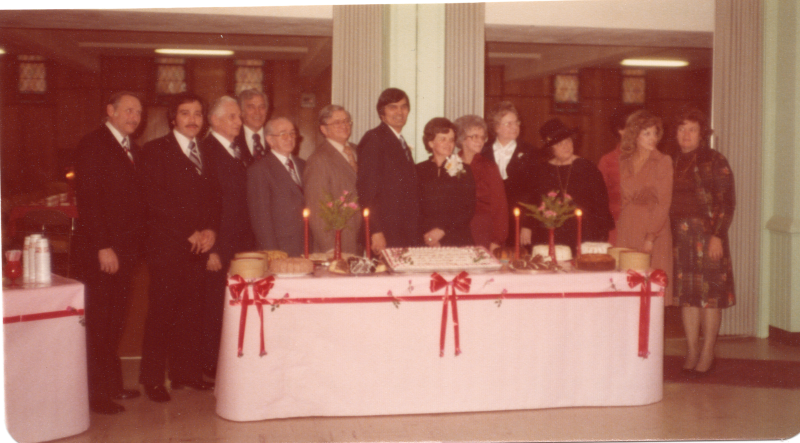 A group of men and women pose in front of a cake