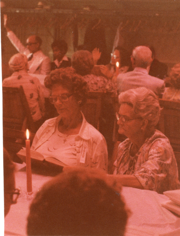 Congregants dining together raise their hands to pray