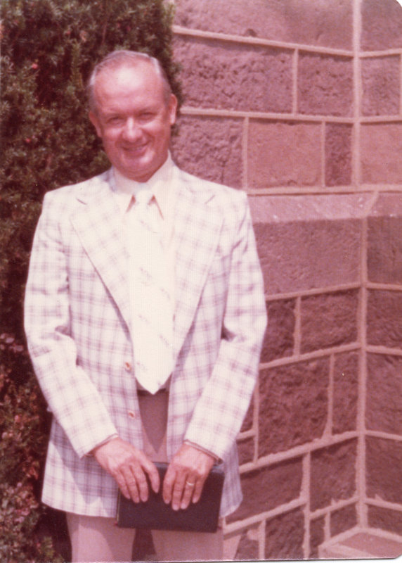 A man dressed in a gingham suit smiles outside of the church building
