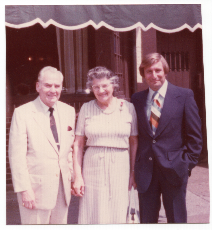 Two men and a women smile together outside of a restaurant