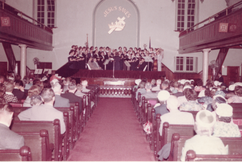 A congregation watches as the choir sings under a "Jesus Saves" cross and crown sign