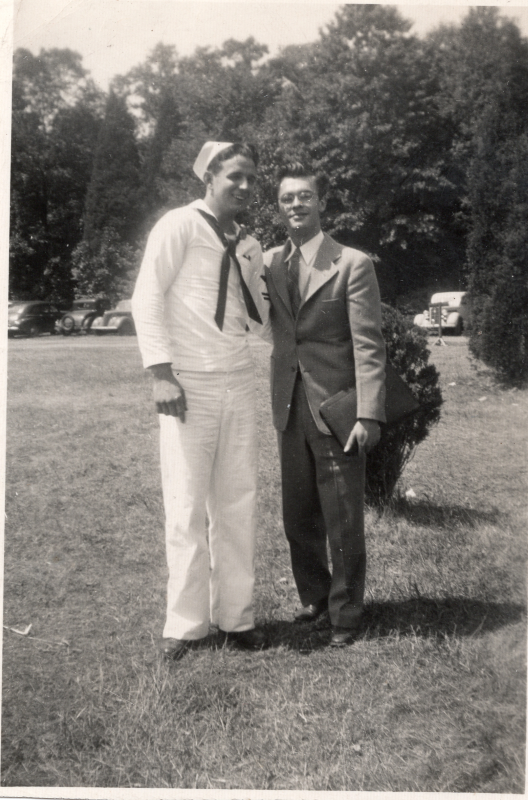A man in a navy suit smiles with a man in a suit