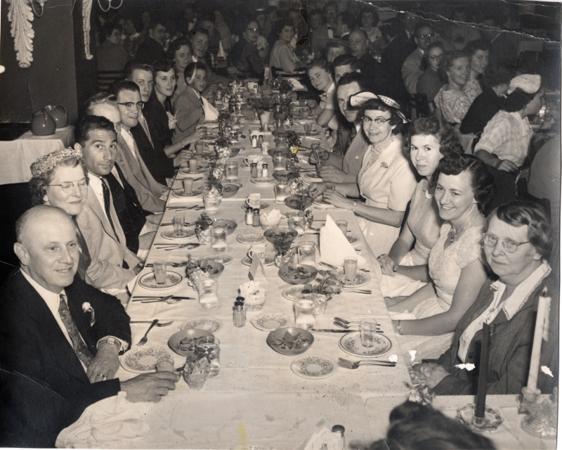 Dozens of congregants seated around dining tables smile for a photograph