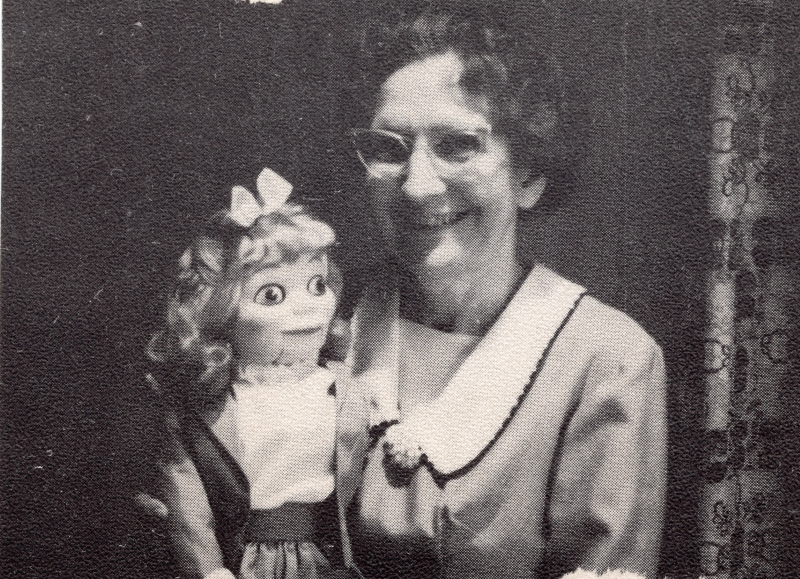 An older woman poses with a female hand puppet