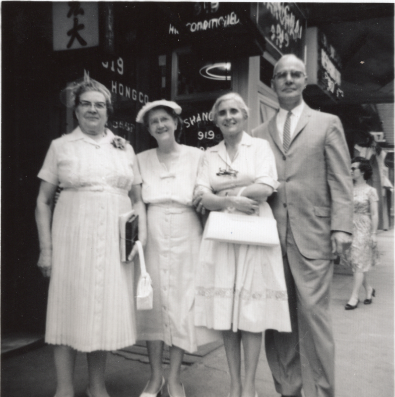 A group of three older women and one man pose for a photograph outside of a store