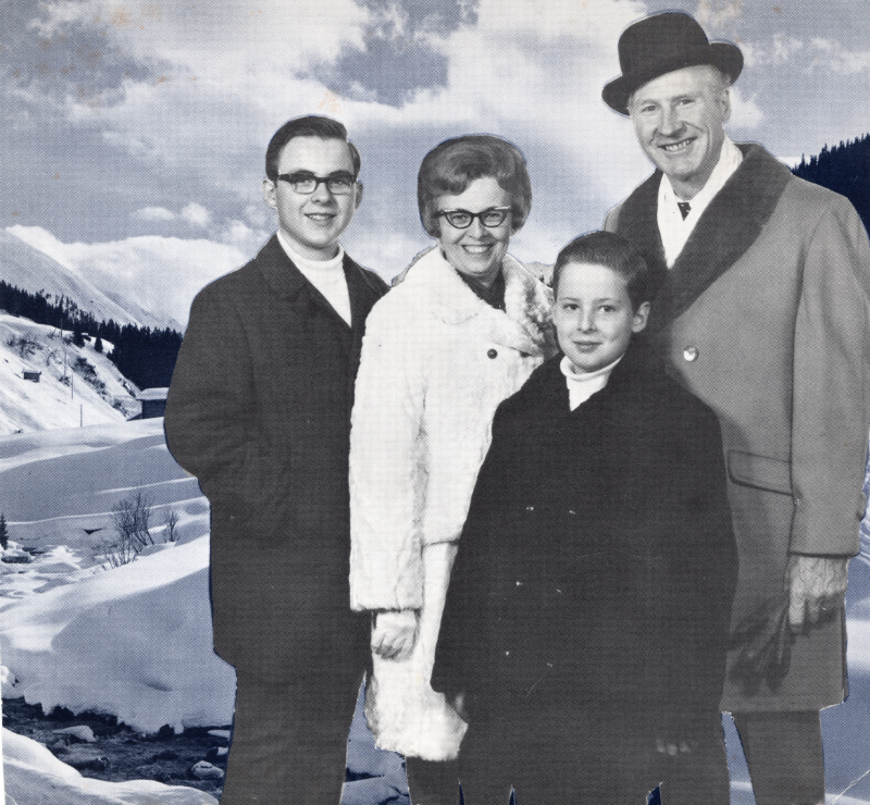 A man, woman, and their two boys smile in front of a snowy mountain backdrop