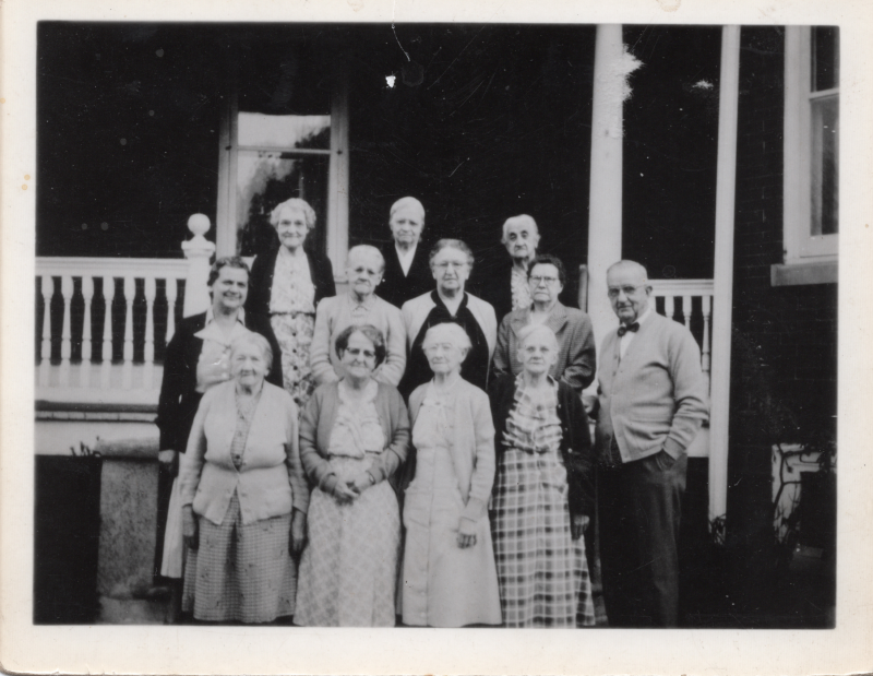 A group of older men and women smile for a group photo outside of Highway Home for the Aged