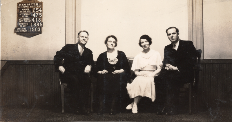 Two women and two men pose together in front of a sign of the the church register