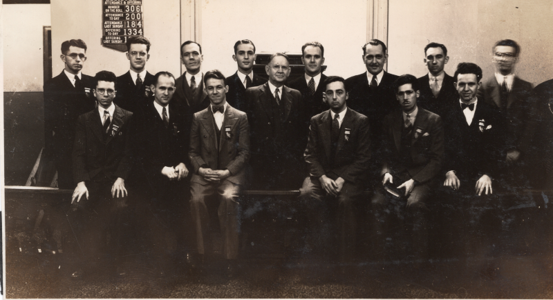 A group of men in suits pose together in front of the church register