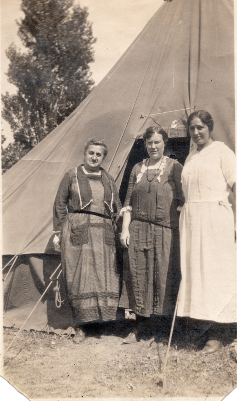 Three women smile together outside of a tent at the Emmanuel Grove Camp