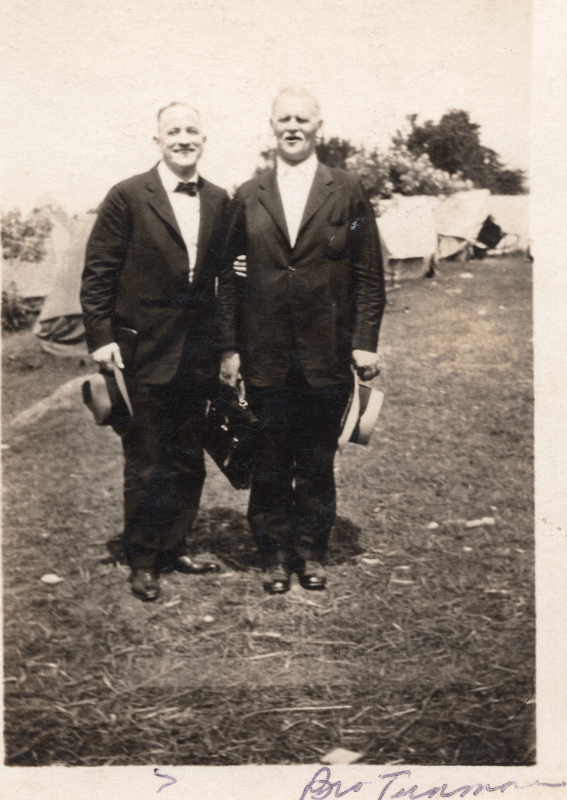 Two men in suits and hats, one named Brother Tannen (sp.?), smile together in front of tents at Emmanuel Grove Camp