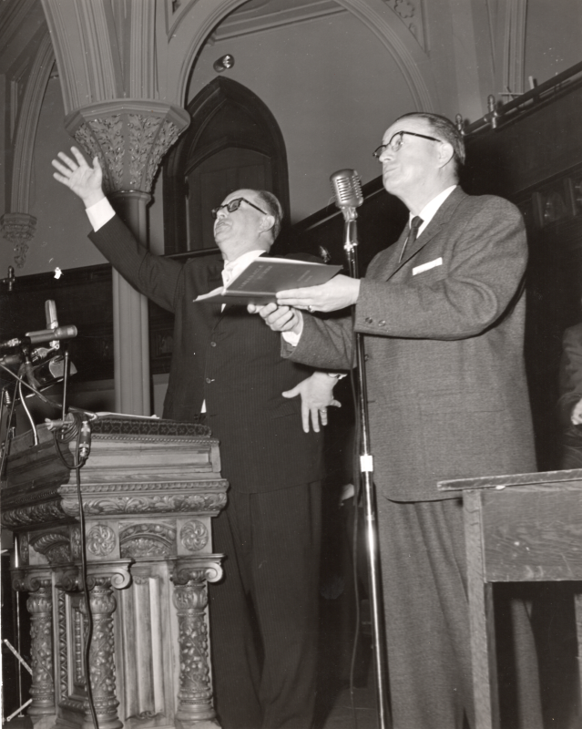 Two men at a microphone in the sanctuary of Highway Tabernacle at 18th and Spring Garden Streets lead the Revivaltime radio broadcast