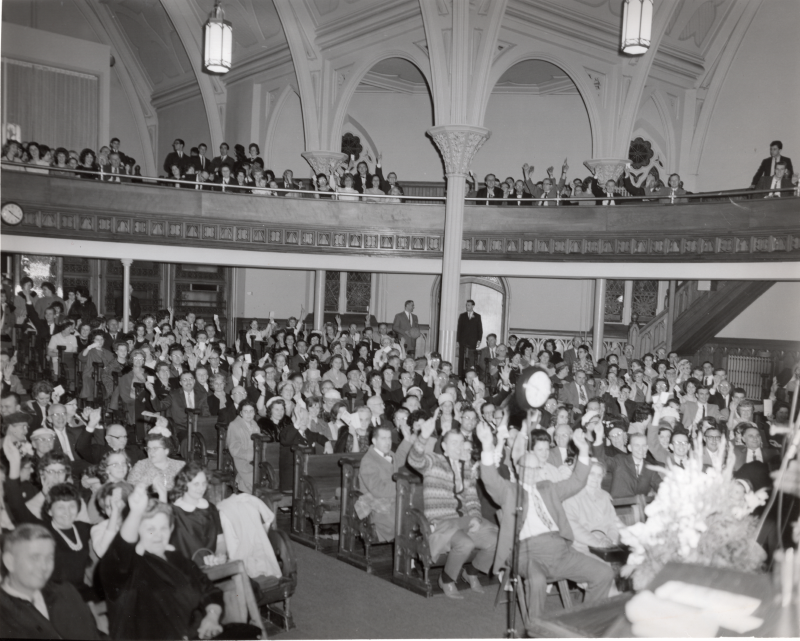 A packed congregation watches the live radio broadcast of Revivaltime with raised hands