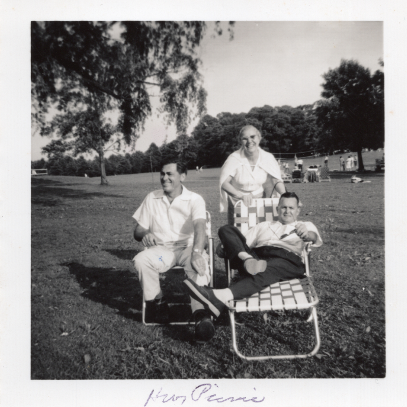 Two men in lawn chairs smile with a standing woman on a field with a caption reading, "HWY Picnic"