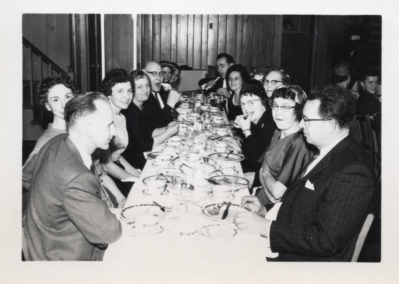 A group of people sit together around a table eating together