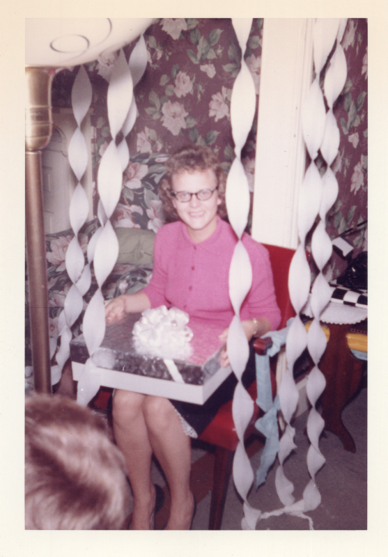 A woman in a pink dress opens a present surrounded by white streamers