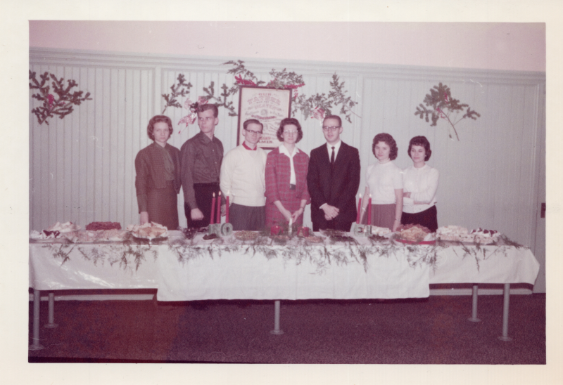 A group of young people stand with Christmas decorations in front of a spread of holiday foods