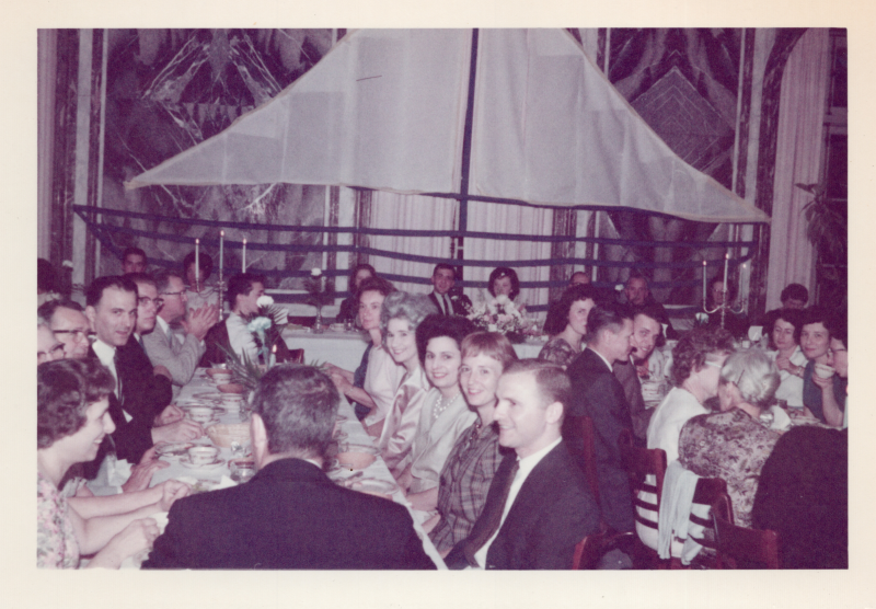Groups sit around tables dining together with a large ship cutout in the background