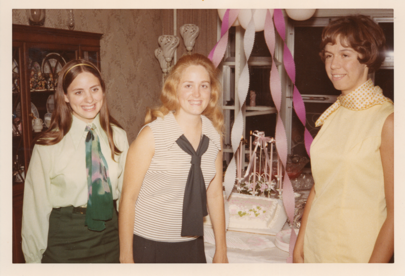 A group of women stand smiling in front of a cake and streamers