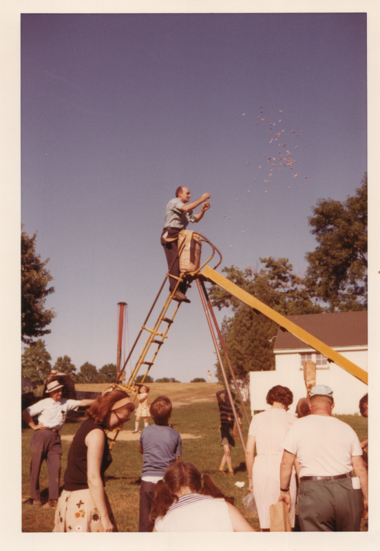 A man throws something from the top of a big yellow slide while adults and children wait on the ground