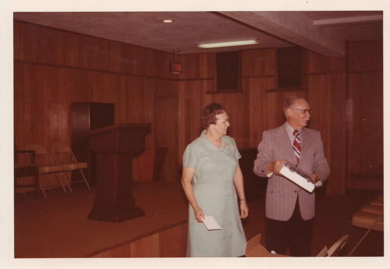 A man and woman walk around together in front of an empty fellowship room