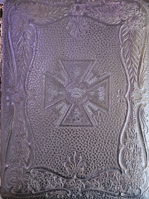 Black leather-bound cover with imagery of a skull and crossbones, an eye with three rings, hands shaking, an other imagery 
