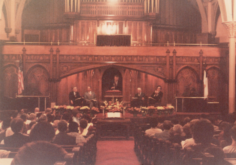 Men on stage in the sanctuary holding Bibles in front of a crowded congregation