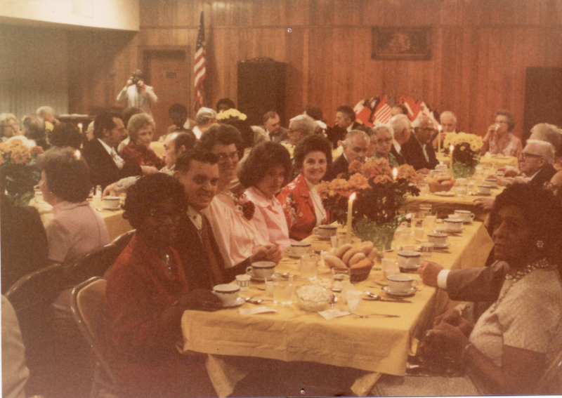 Congregants dine together with world flags in the background