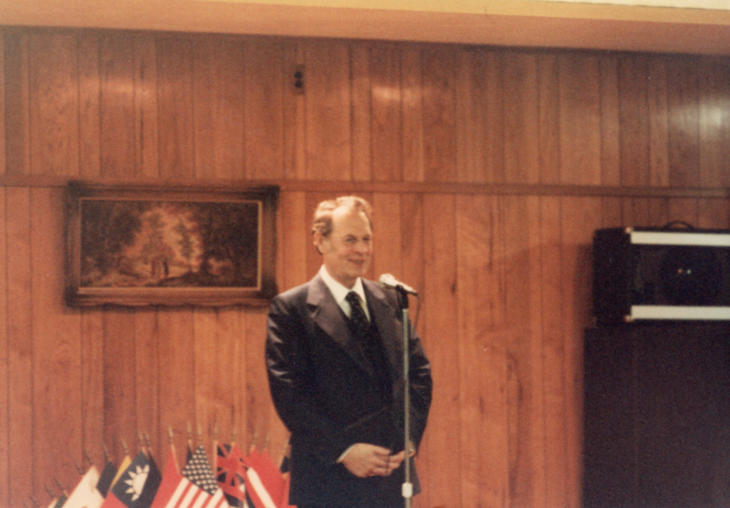 A man standing in front of world flags addresses diners