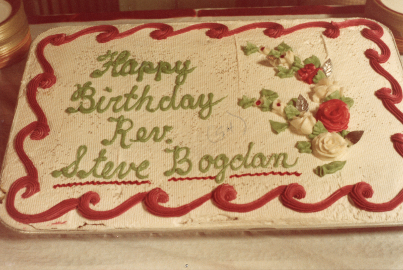 Pastor Bogdan's birthday cake reading, "Happy Birthday Rev. Steve Bogdan" with red and green floral detail. The text "(54)" has been added to the image with pen