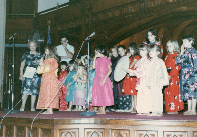 Children in international outfits sing together on stage in the sanctuary